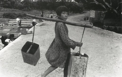 一斗缶で水を運ぶ少女